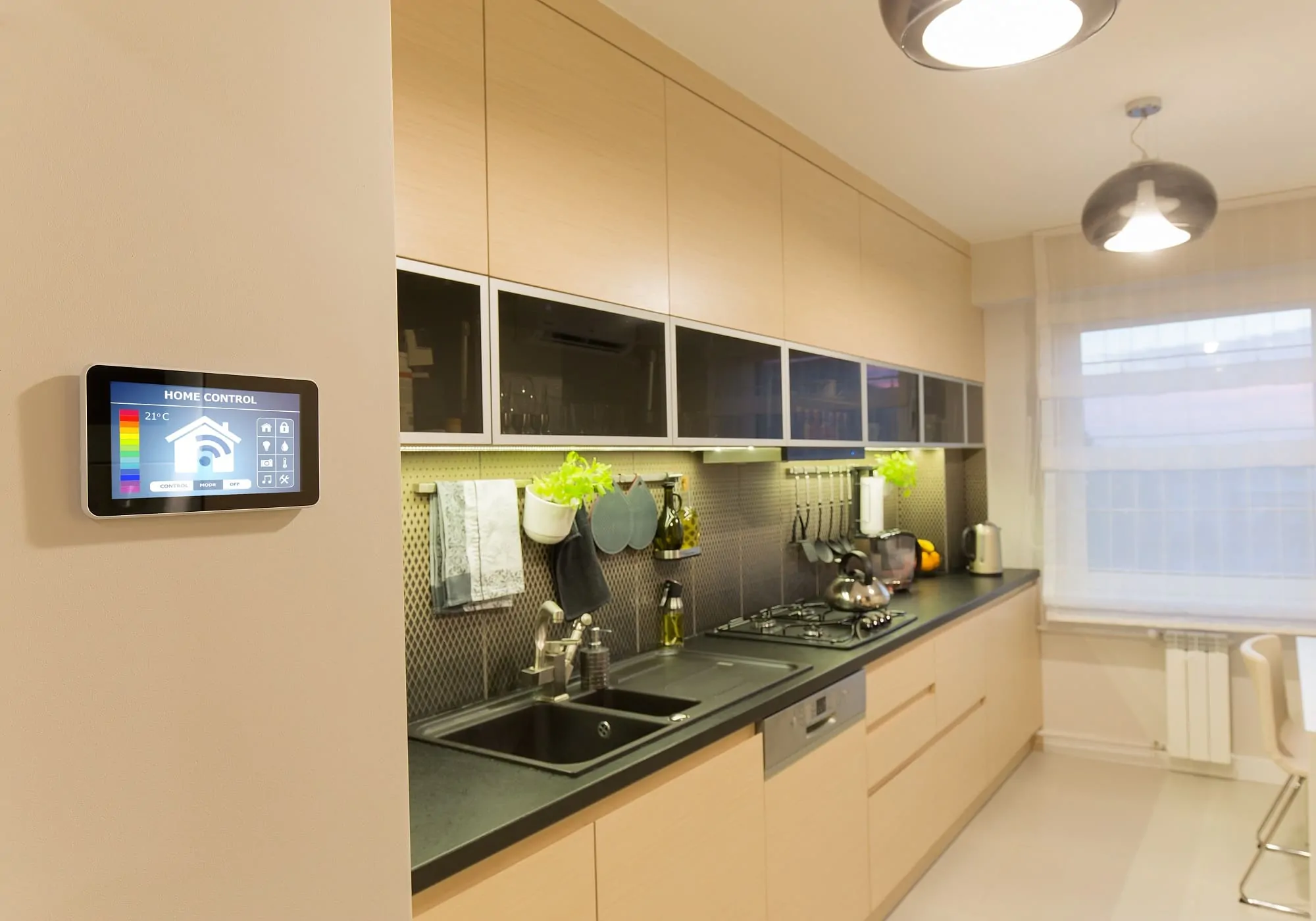 Modern kitchen with light wood cabinets, smart home control panel for C-Bus maintenance, appliances, and under-cabinet lights.